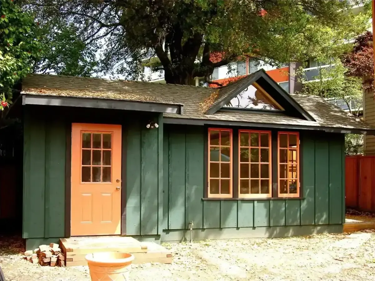 Board-and-batten ADU with orange door under a heritage tree