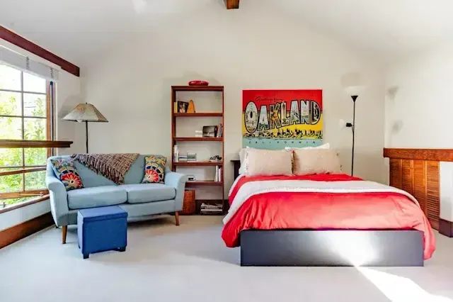 Vaulted bedroom with exposed beams, mid-century sofa, and Oakland artwork