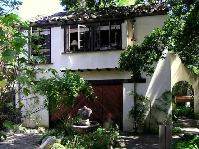 Spanish-revival stucco home with tile roof, wood garage door, and stone fountain in the front garden