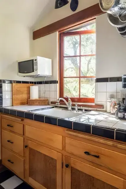 Cottage kitchen with tiled counters, exposed beam, and divided-light window over the sink