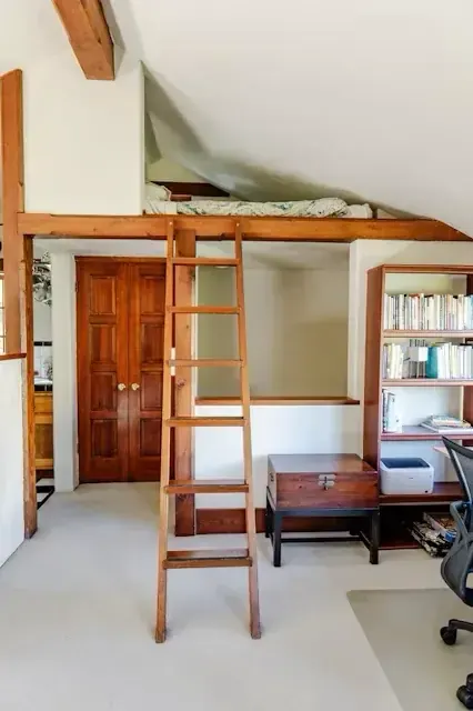 Sleeping loft with handcrafted wood ladder, exposed beams, and built-in bookshelves